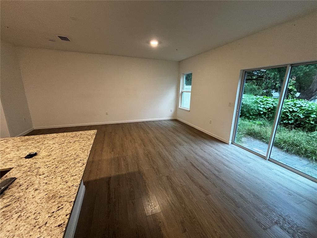 An open living area features wood-look flooring, a granite-topped island, and sliding glass doors — 1209 SOUTHSTATION PLACE UNIT 303, ORLANDO, FL