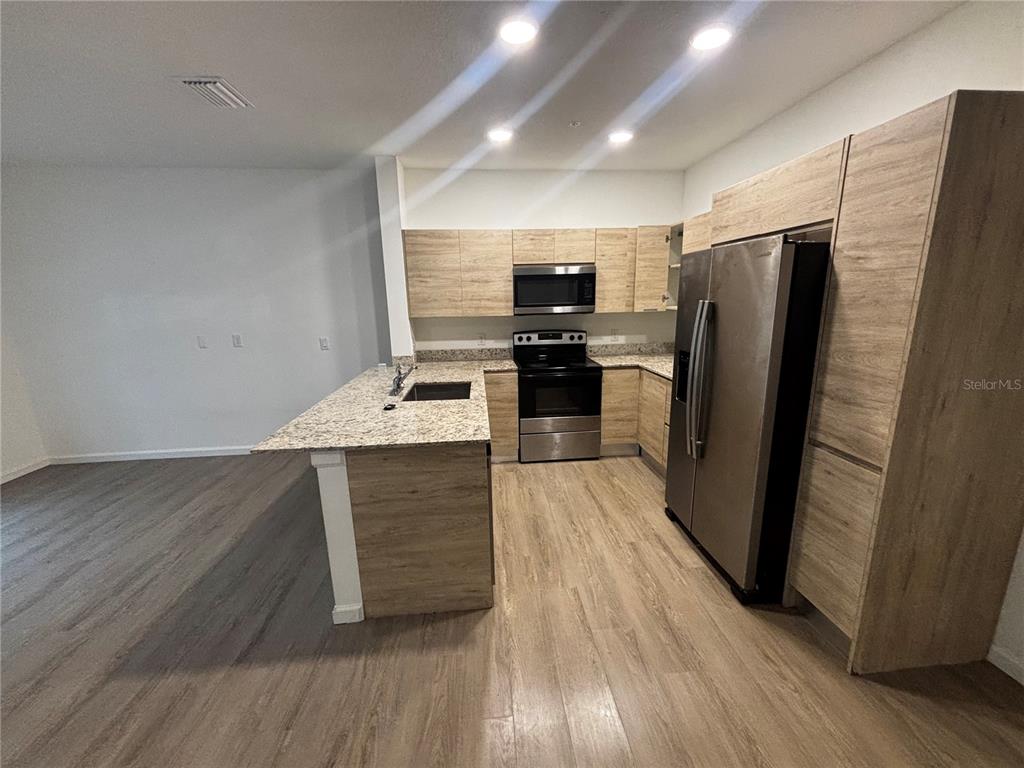 A kitchen features light wood cabinets, stainless steel appliances, and a granite-topped island — 1209 SOUTHSTATION PLACE UNIT 303, ORLANDO, FL