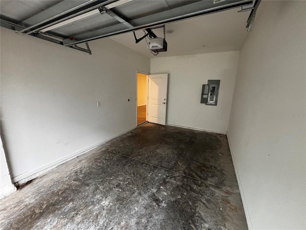 An empty garage features a concrete floor, a ceiling-mounted opener, and an interior door — 1209 SOUTHSTATION PLACE UNIT 303, ORLANDO, FL