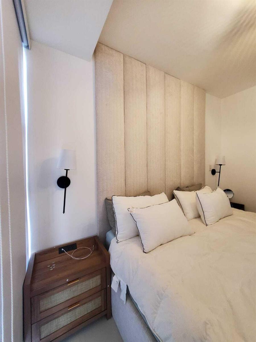A bedroom features a tall, vertical-paneled upholstered headboard, two wooden nightstands, and wall-mounted sconces — 50 C. Los Fereira # I8, FL