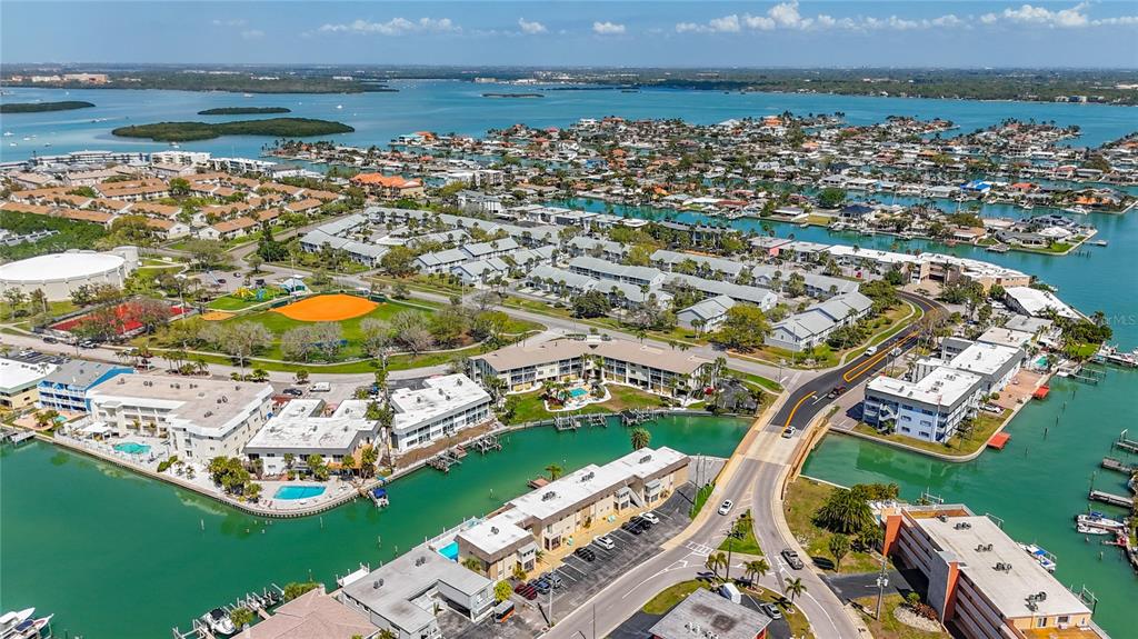 An aerial view shows waterfront apartment buildings, a baseball field, and a bridge over water — 184 117TH AVENUE UNIT 2, TREASURE ISLAND, FL