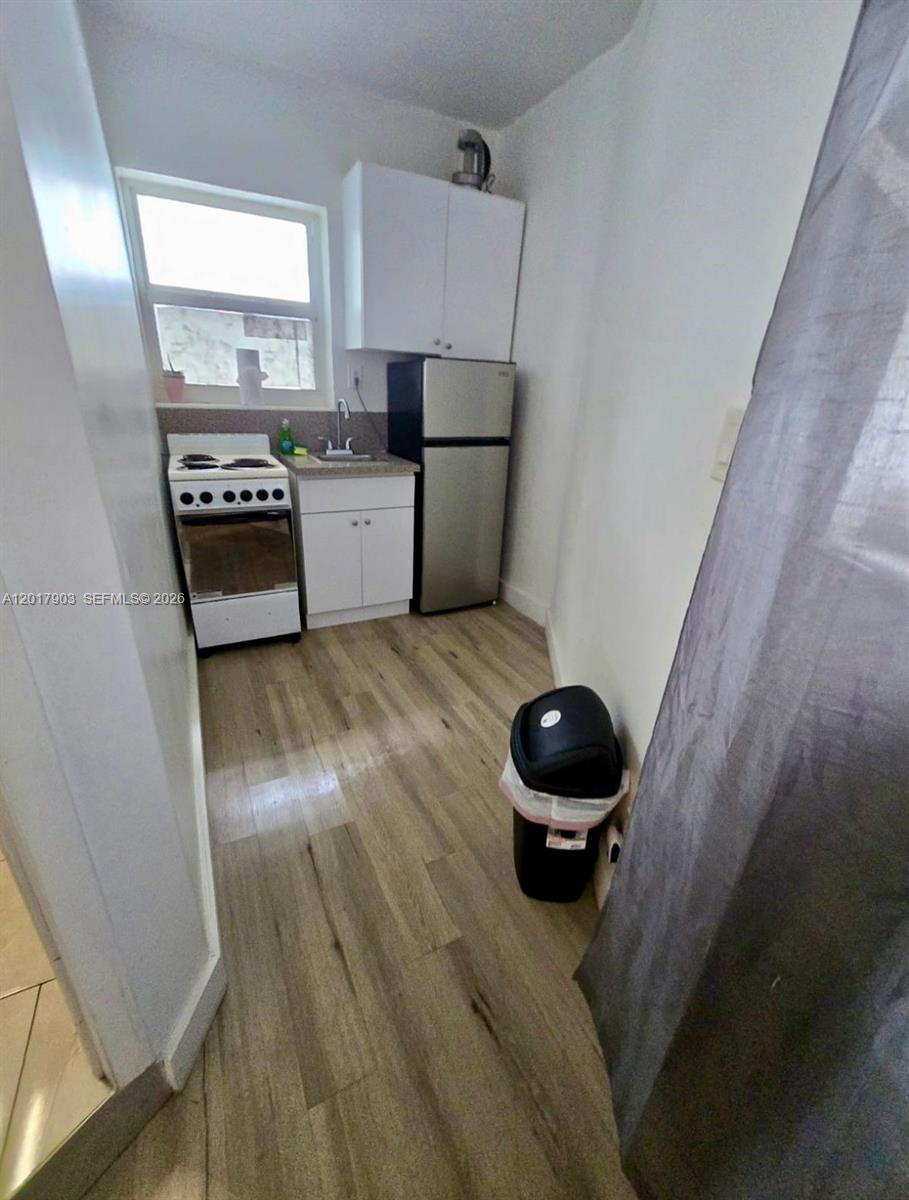 A small kitchen features white cabinets, a stainless steel refrigerator, a stove, and wood-look flooring — 109 SE 9th St # 6, Hallandale Beach FL 33009, HALLANDALE BEACH, FL