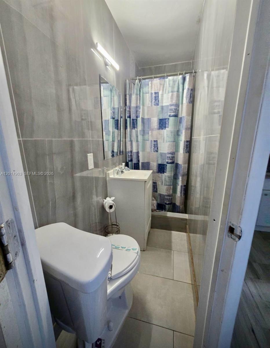 A small bathroom features gray tiled walls, a white pedestal sink, and a shower curtain — 109 SE 9th St # 6, Hallandale Beach FL 33009, HALLANDALE BEACH, FL