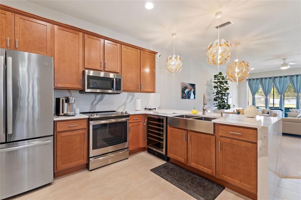 A kitchen features wood cabinets, stainless steel appliances, a farmhouse sink, and marble-look countertops — 1678 LINZ COURT, WINTER HAVEN, FL