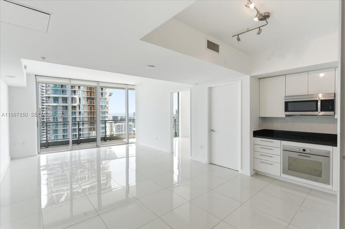 A modern kitchen with white cabinets and black countertops opens into a bright living area — 92 SW 3rd St # 3804, Miami FL 33130, MIAMI, FL