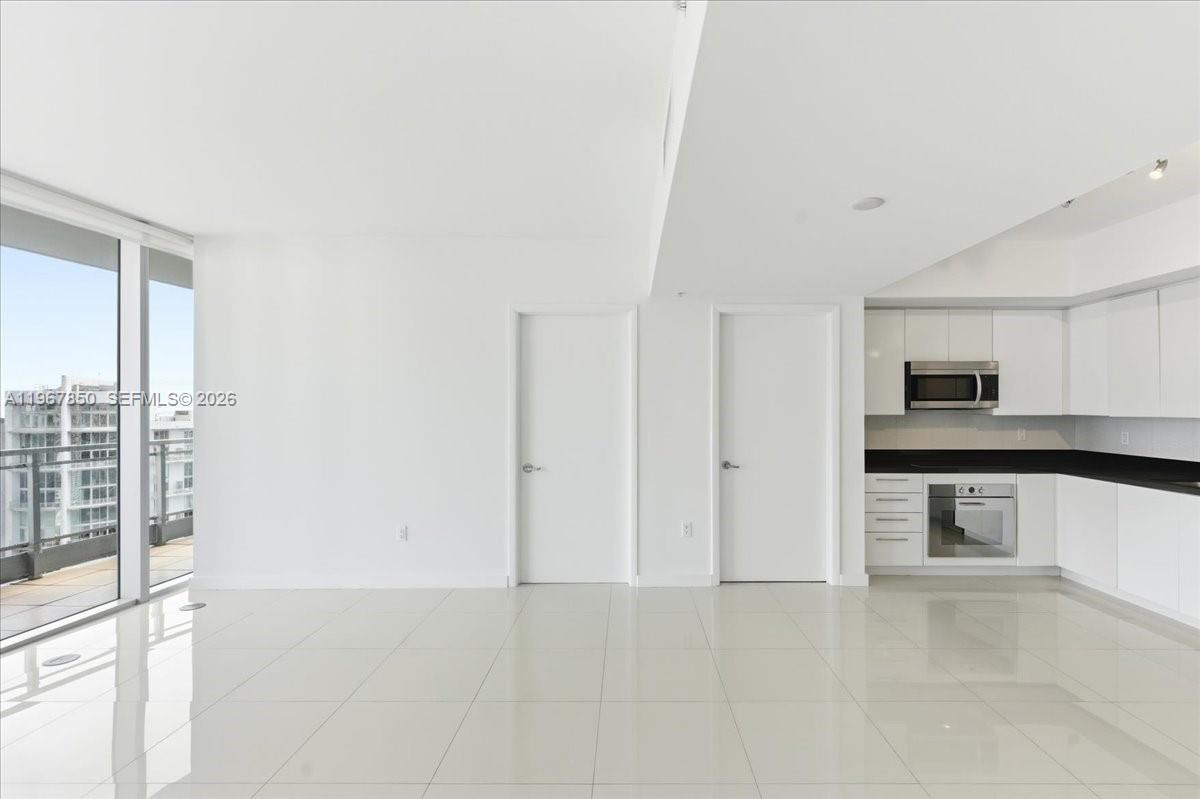 A modern, minimalist kitchen with white cabinetry and tile flooring opens into a bright living area — 92 SW 3rd St # 3804, Miami FL 33130, MIAMI, FL
