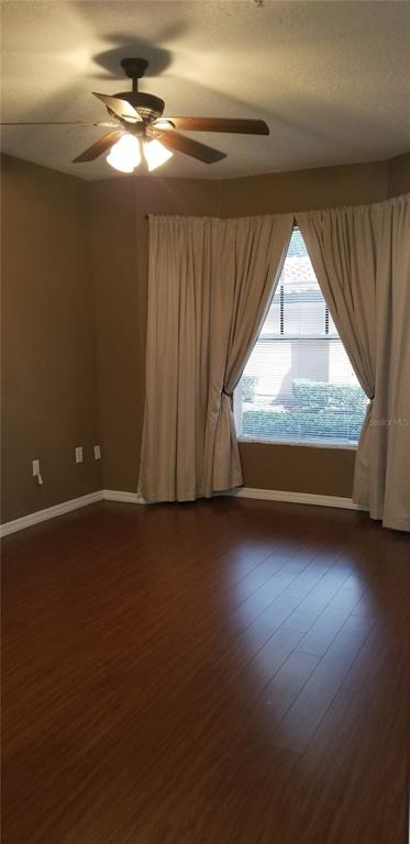 An empty room with dark wood flooring, beige walls, a ceiling fan, and window curtains — 5542 METROWEST BOULEVARD UNIT 106, ORLANDO, FL