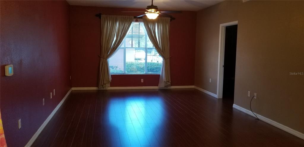 An empty room features dark wood flooring, a ceiling fan, and a window with curtains — 5542 METROWEST BOULEVARD UNIT 106, ORLANDO, FL
