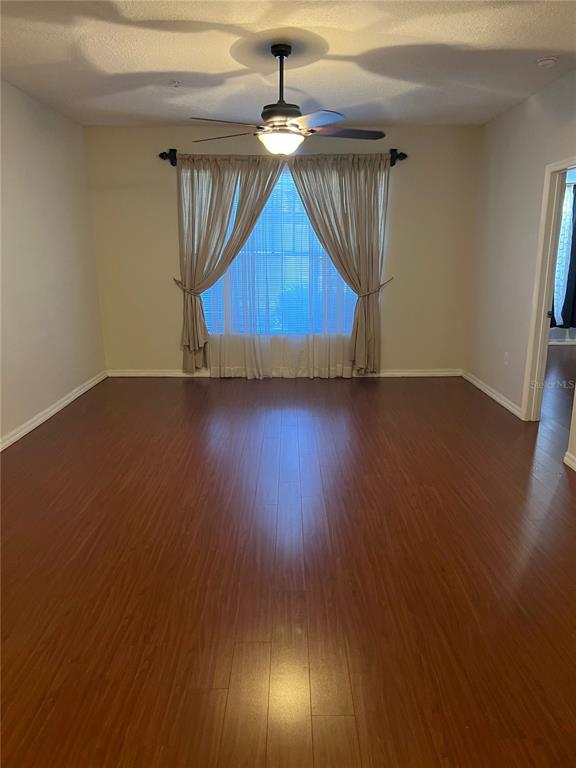 An empty room features wood-look flooring, a ceiling fan, and curtains covering a large window — 5542 METROWEST BOULEVARD UNIT 106, ORLANDO, FL