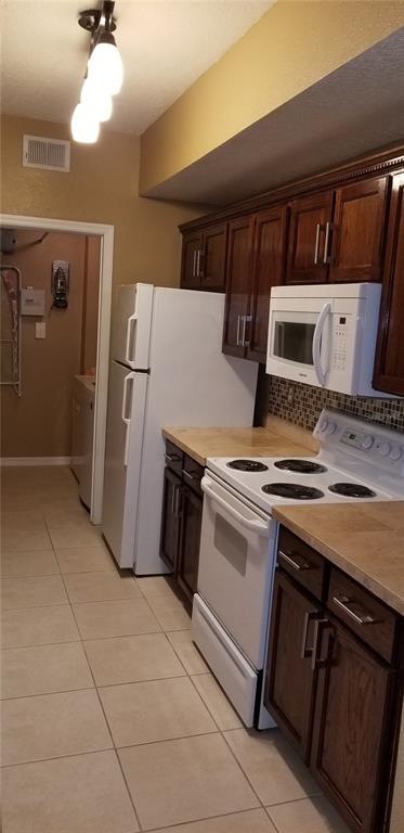 A kitchen features dark wood cabinets, white appliances, tile flooring, and a light-colored countertop — 5542 METROWEST BOULEVARD UNIT 106, ORLANDO, FL