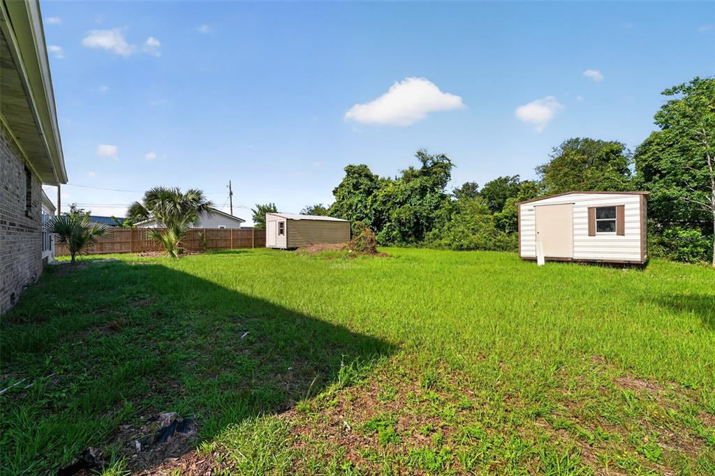 A grassy backyard features two storage sheds and a wooden fence under a blue sky — 219 N EAST AVENUE, PANAMA CITY, FL