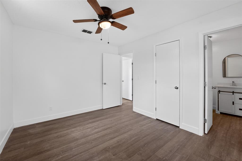 A bedroom with white walls, wood-look flooring, a ceiling fan, and an attached bathroom — 219 N EAST AVENUE, PANAMA CITY, FL