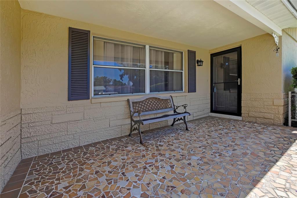 A covered front porch features a mosaic tile floor, a metal bench, and stone siding — 3632 MORLEY DRIVE, NEW PORT RICHEY, FL