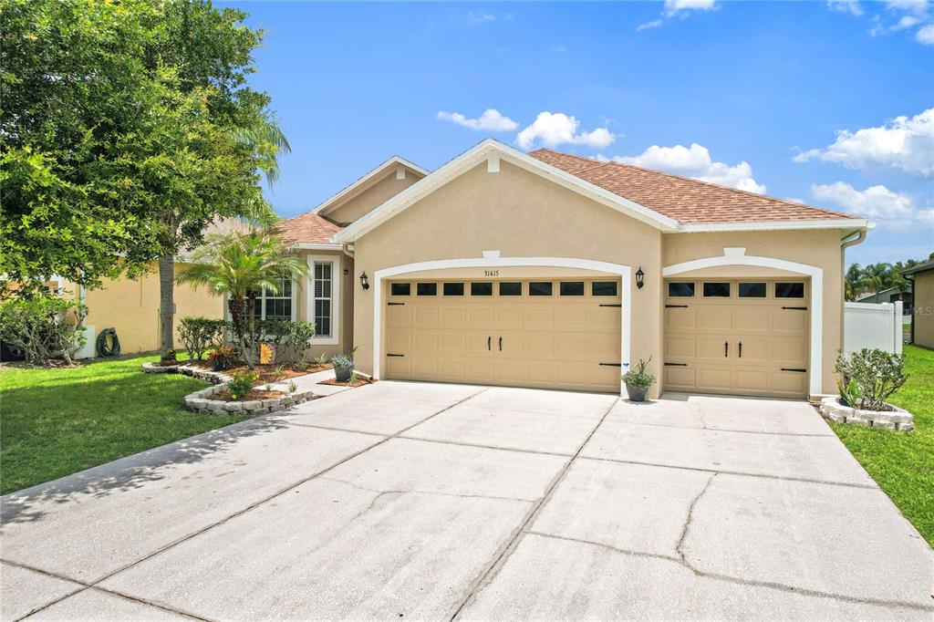A single-story suburban house with a tan stucco exterior and a two-car garage — 31415 BRIDGEGATE DRIVE, WESLEY CHAPEL, FL