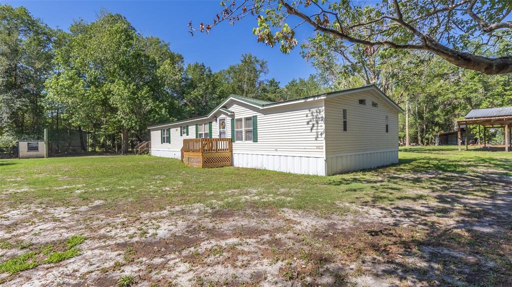 A single-story manufactured home with light siding, green shutters, and a wooden front deck — 17824 NE 143RD TERRACE, WALDO, FL