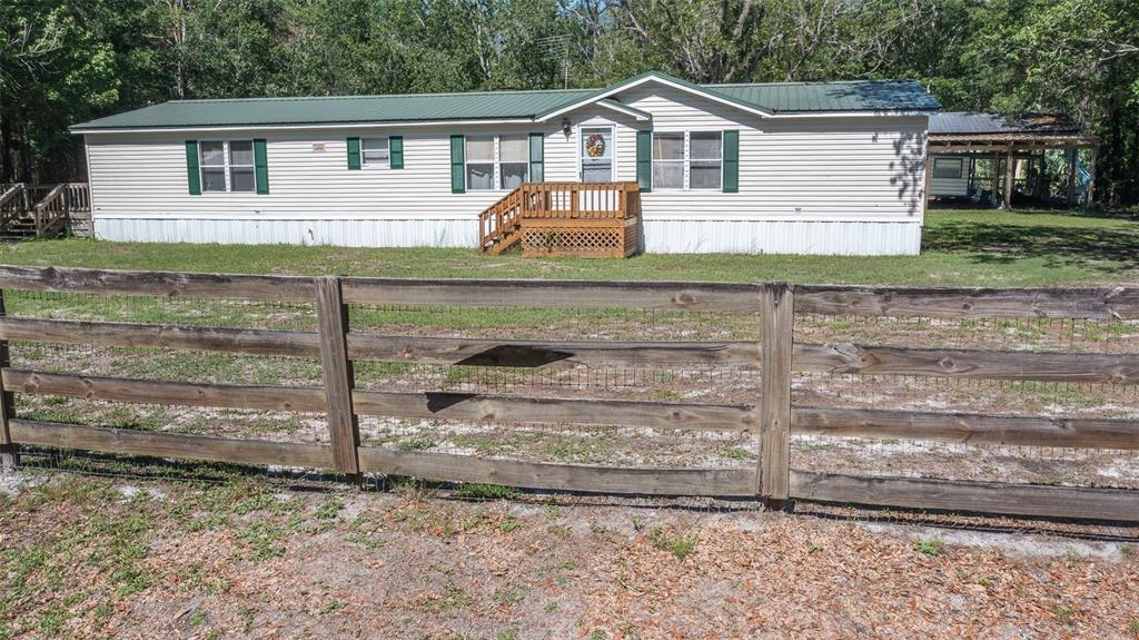 A single-story manufactured home with a green metal roof sits behind a wooden fence — 17824 NE 143RD TERRACE, WALDO, FL