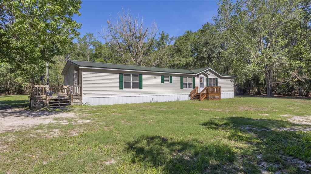 A single-story manufactured home with beige siding and a green metal roof sits on grass — 17824 NE 143RD TERRACE, WALDO, FL