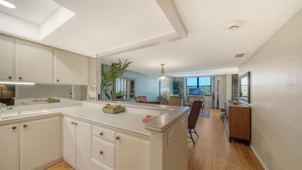 A kitchen with white cabinets and a breakfast bar overlooks a living and dining area — 8773 MIDNIGHT PASS ROAD UNIT 302G, SARASOTA, FL
