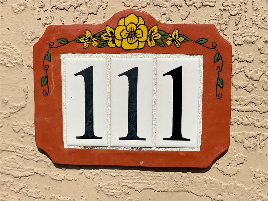 A decorative ceramic plaque with the number 111 mounted on a textured stucco wall — 12102 POPPY FIELD LANE UNIT 111, ORLANDO, FL