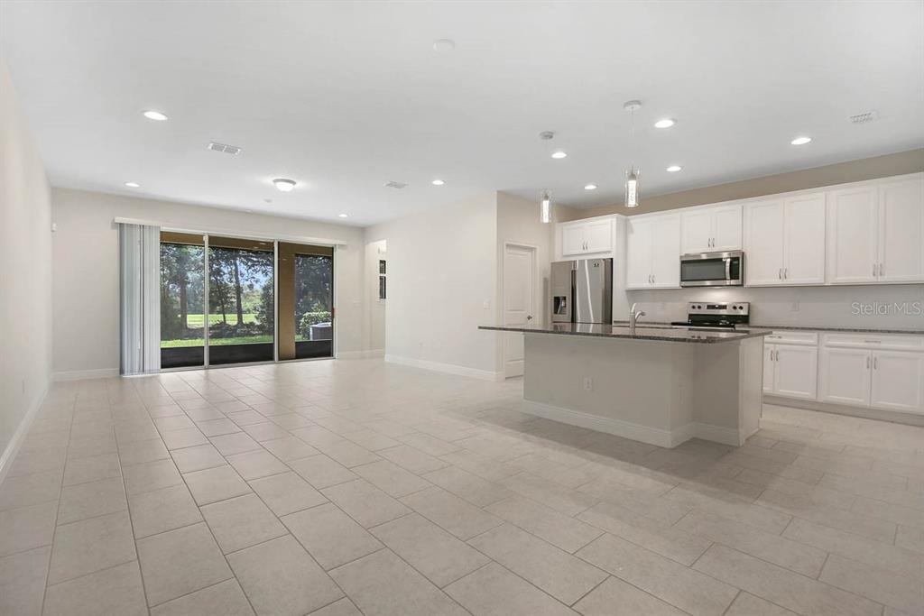 An open-concept kitchen and living area features white cabinetry, a granite island, and tile flooring — 10232 NEWEL VALLEY LOOP, RIVERVIEW, FL