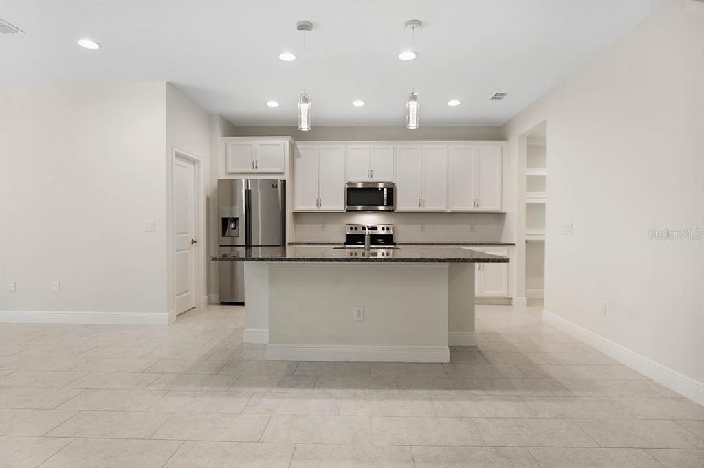 A modern kitchen features white cabinetry, stainless steel appliances, a granite island, and tile flooring — 10232 NEWEL VALLEY LOOP, RIVERVIEW, FL