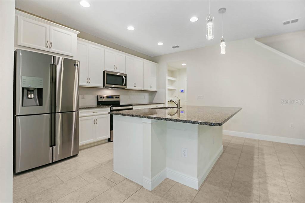 A kitchen features white cabinets, stainless steel appliances, a granite-topped island, and tile flooring — 10232 NEWEL VALLEY LOOP, RIVERVIEW, FL