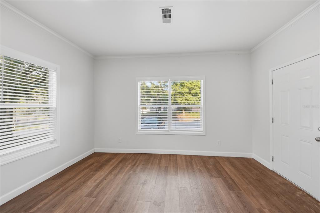 An empty room features light gray walls, wood-look flooring, two windows with blinds, and a door — 5430 ROSE AVENUE, ORLANDO, FL