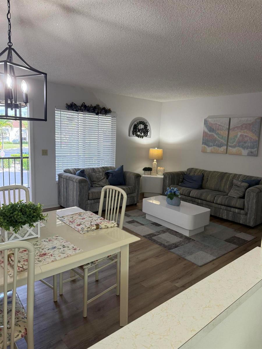 A living room and dining area feature wood-look flooring, neutral walls, and a modern chandelier — 133 Lake Pine Circle # 2, FL 33463, FL
