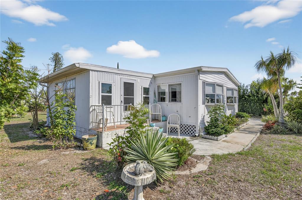 A white mobile home with a small porch and patio sits on a grassy lot — 1349 SEAGULL DRIVE, ENGLEWOOD, FL