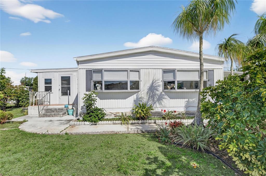 A single-story manufactured home with white siding, bay windows, and a palm tree in front — 1349 SEAGULL DRIVE, ENGLEWOOD, FL