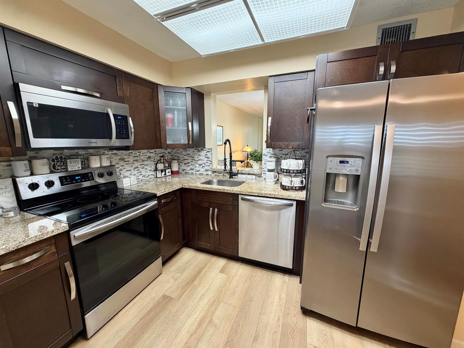 A kitchen features dark wood cabinets, stainless steel appliances, granite countertops, and light wood flooring — 7320 Lake Cir Drive # 204, Margate FL 33063, MARGATE, FL