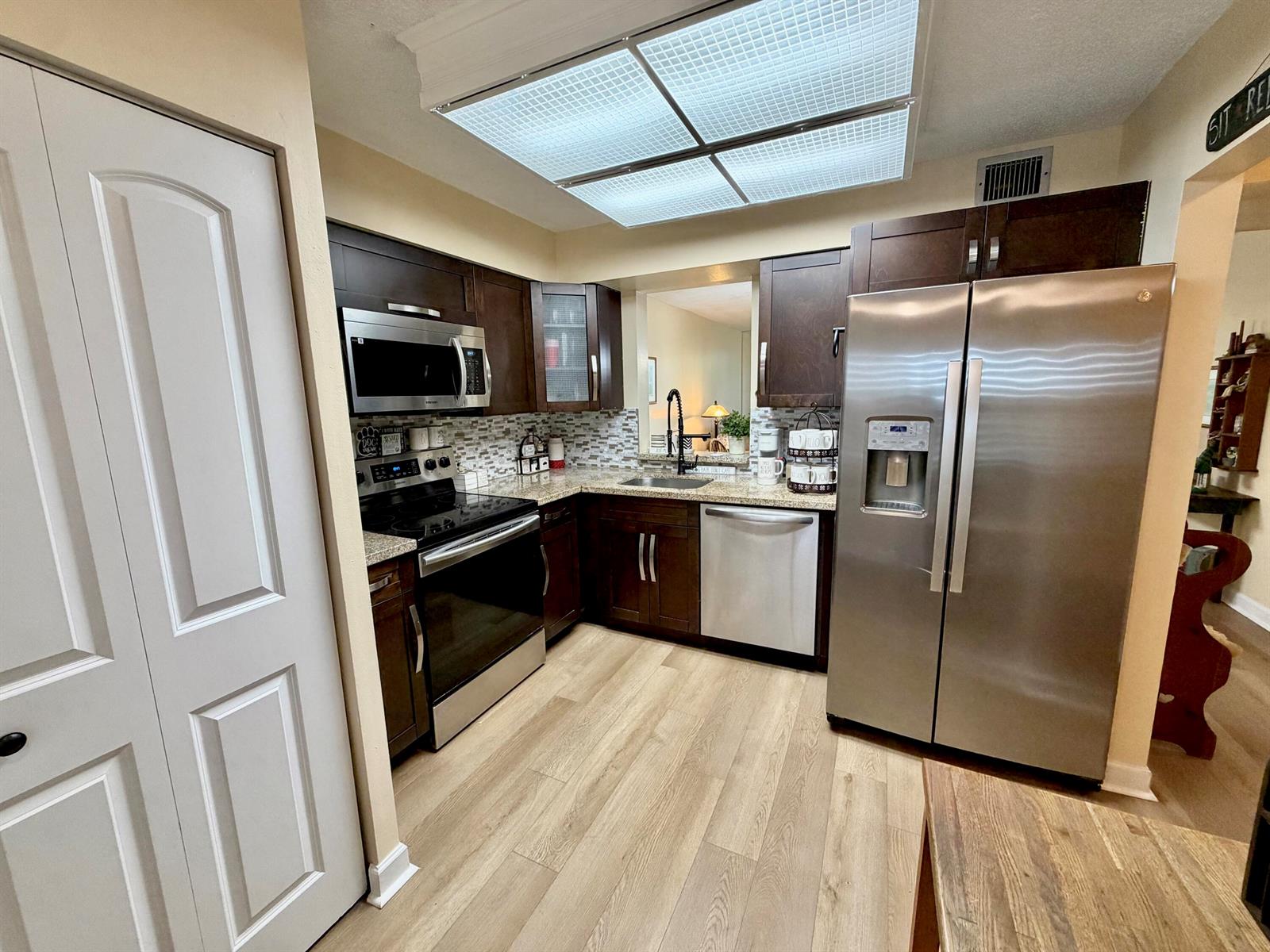 A kitchen features dark wood cabinets, stainless steel appliances, light countertops, and wood-look flooring — 7320 Lake Cir Drive # 204, Margate FL 33063, MARGATE, FL