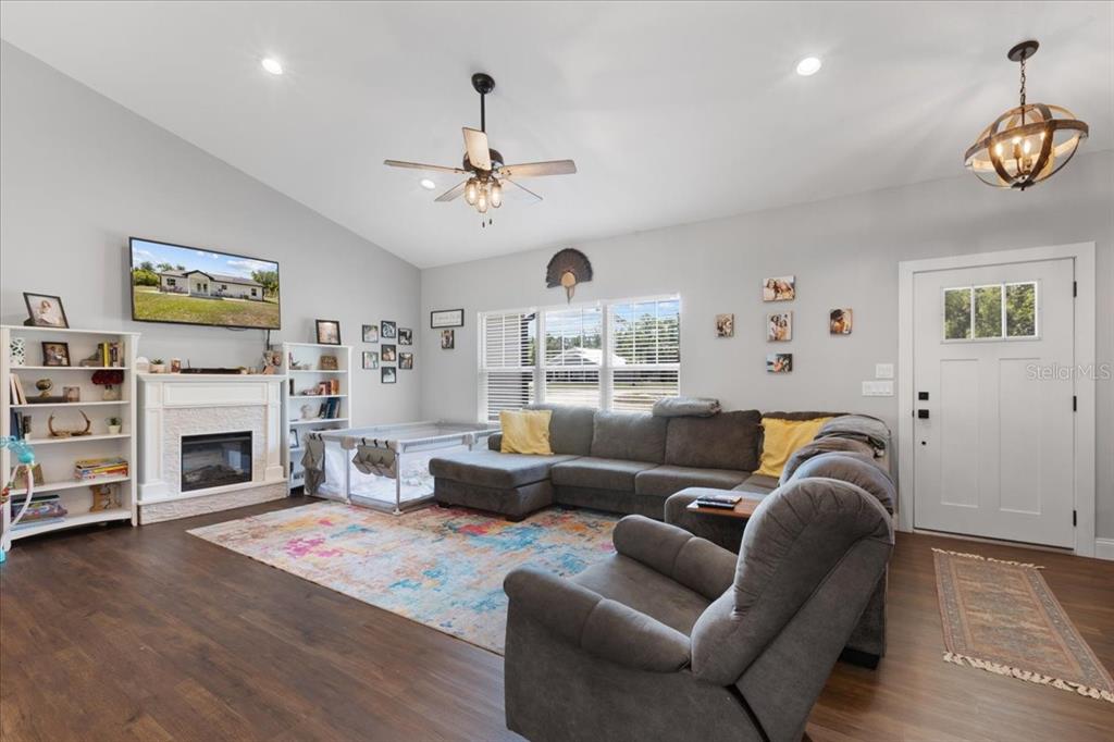 A living room with wood-look flooring, a sectional sofa, a fireplace, and a ceiling fan — 5231 NW 73RD STREET, CHIEFLAND, FL