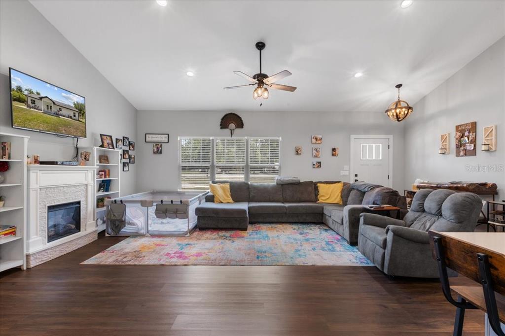 A living room features a fireplace, a large sectional sofa, a playpen, and wood flooring — 5231 NW 73RD STREET, CHIEFLAND, FL