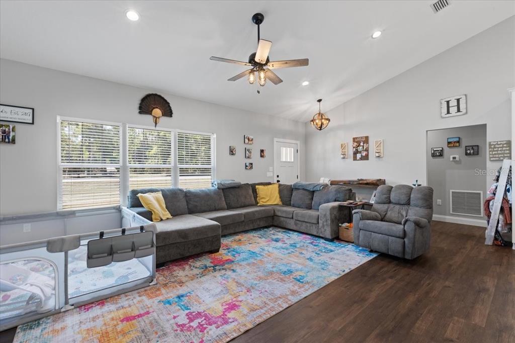 A living room features a gray sectional sofa, a recliner, and a colorful area rug — 5231 NW 73RD STREET, CHIEFLAND, FL
