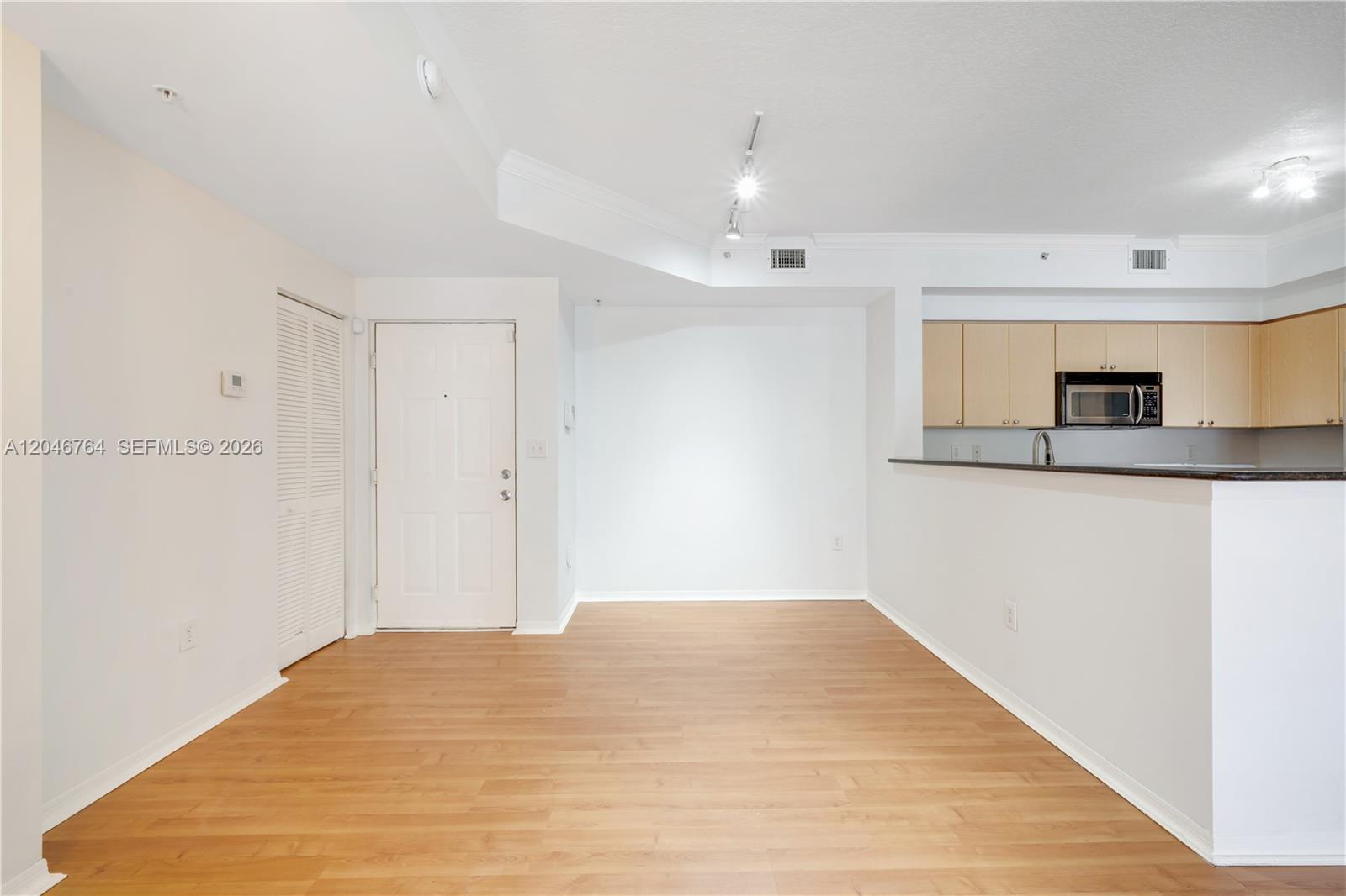 An empty room with light wood flooring, a white door, and an open kitchen area — 6851 SW 44th St # 208, Miami FL 33155, MIAMI, FL