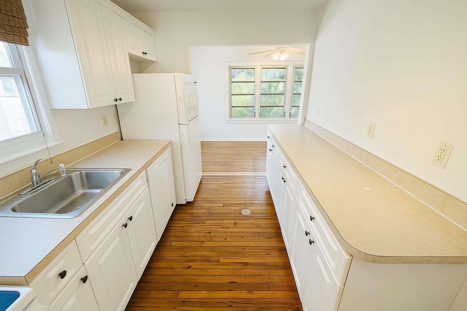 A galley kitchen with white cabinets, laminate countertops, and hardwood flooring leads to a dining area — 415 6th Avenue N, FL 33460, FL