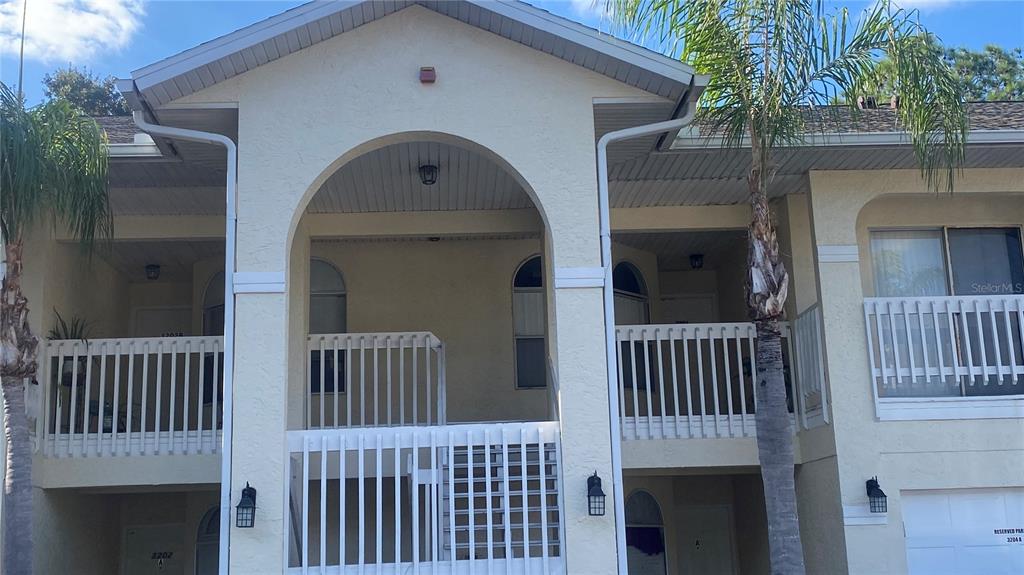 The exterior of a two-story apartment building features a central arched entryway and balconies — 3204 SABAL PALMS COURT UNIT B, KISSIMMEE, FL