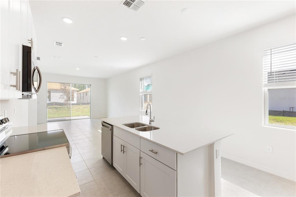 A modern kitchen features white cabinets, a quartz island with a sink, and tile flooring — 2031 ANTHEM DRIVE, ORANGE CITY, FL
