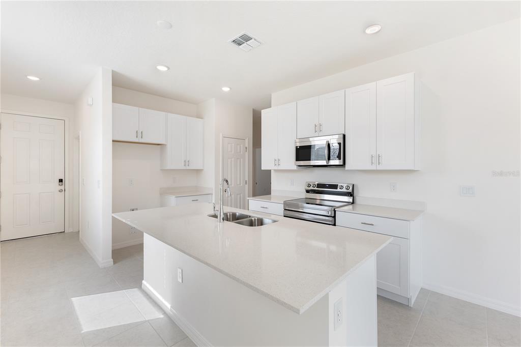 A modern kitchen features white cabinetry, a large quartz island, and stainless steel appliances — 2031 ANTHEM DRIVE, ORANGE CITY, FL