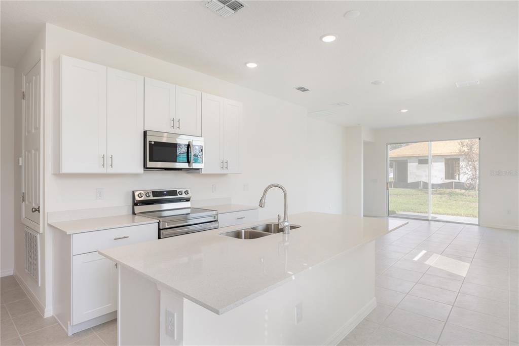 A modern kitchen features white cabinets, stainless steel appliances, a quartz island, and tile flooring — 2031 ANTHEM DRIVE, ORANGE CITY, FL