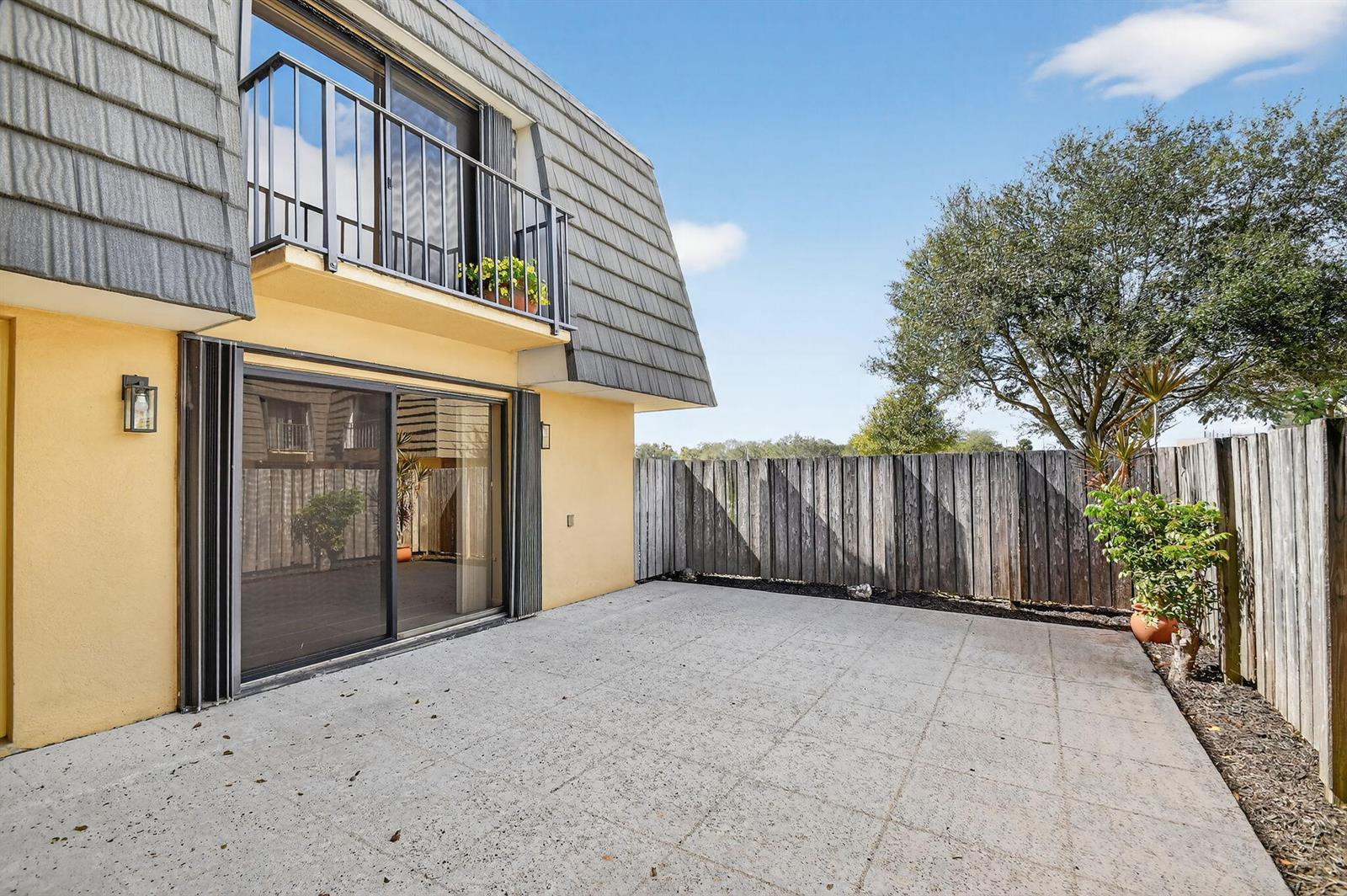 A concrete patio sits outside a two-story building with a sliding glass door and balcony — 4210 42nd Way, West Palm Beach FL 33407, WEST PALM BEACH, FL