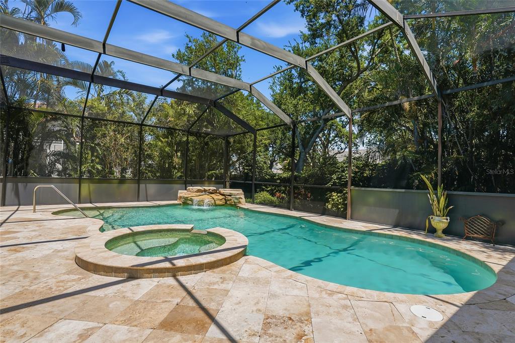 A screened-in swimming pool and spa with a stone waterfall feature and travertine patio — 777 CATTAIL COURT NE, ST PETERSBURG, FL
