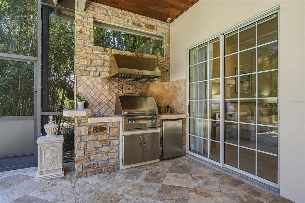 An outdoor kitchen features a stone grill station, stainless steel appliances, and a sliding glass door — 777 CATTAIL COURT NE, ST PETERSBURG, FL