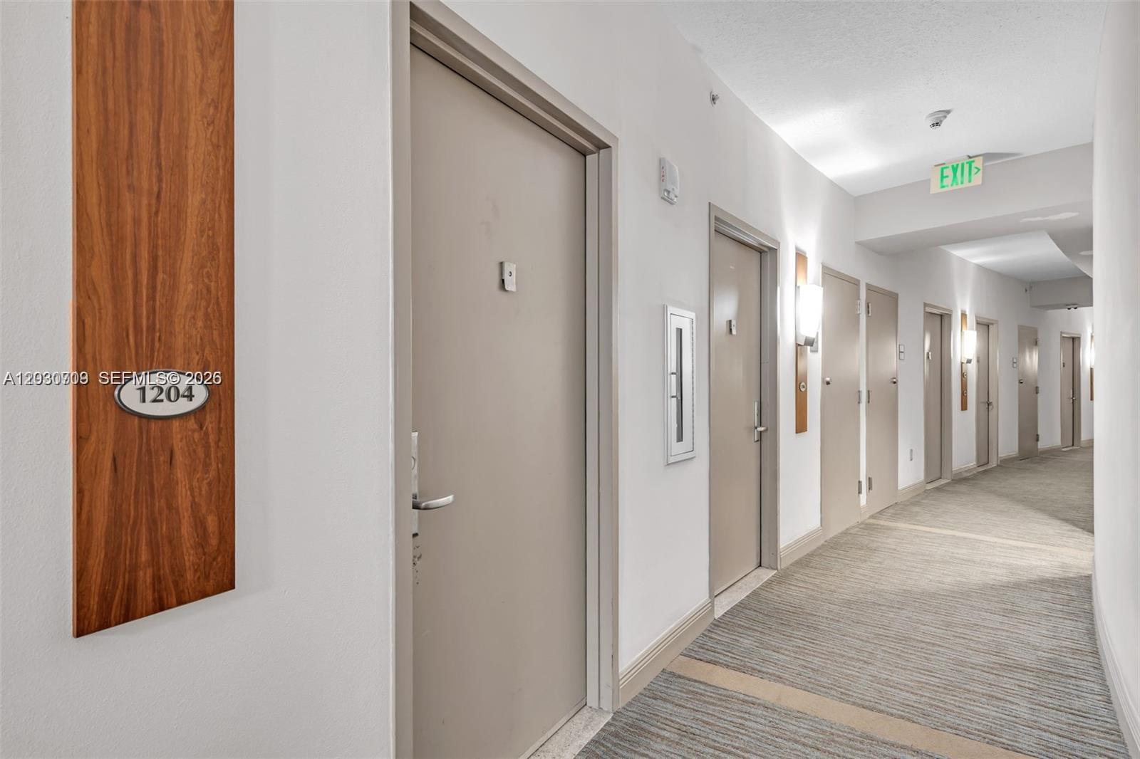 A long apartment building hallway features beige doors, white walls, and a striped carpet — 1750 N Bayshore Dr # 1204, Miami FL 33132, MIAMI, FL