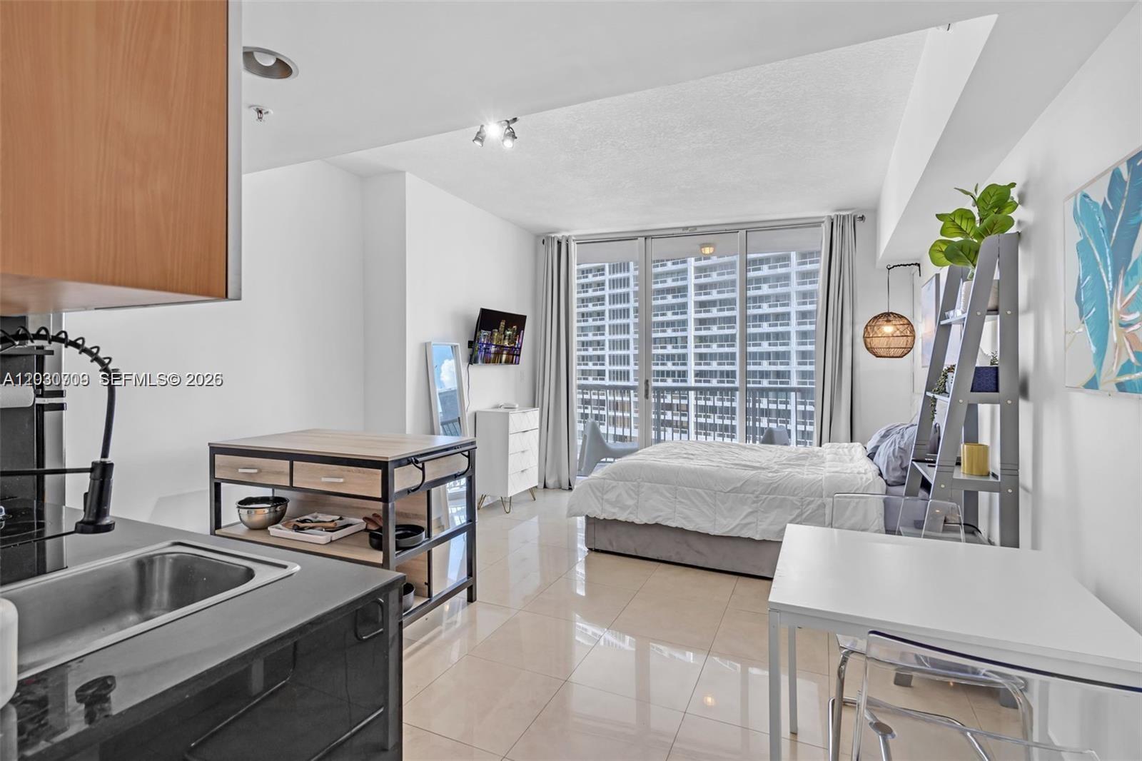 A studio apartment features a kitchen island, a bed, and a view of high-rise buildings — 1750 N Bayshore Dr # 1204, Miami FL 33132, MIAMI, FL