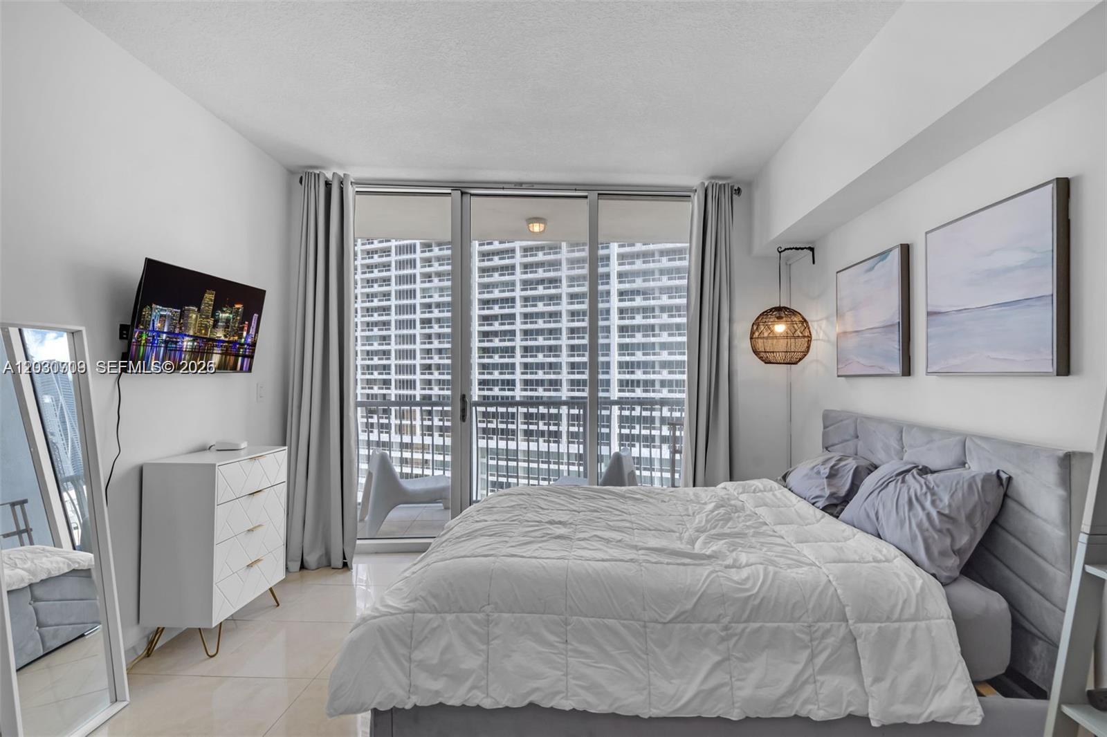 A modern bedroom features a bed, dresser, wall-mounted television, and a balcony with city views — 1750 N Bayshore Dr # 1204, Miami FL 33132, MIAMI, FL