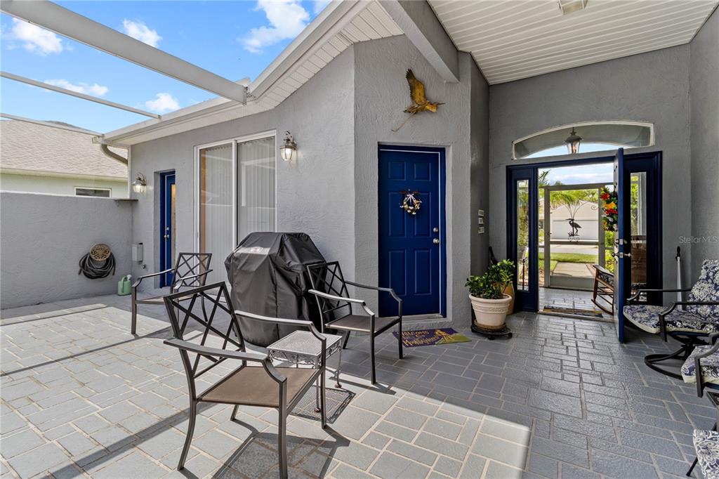 A covered patio with gray pavers, a blue door, and outdoor furniture — 3007 BELLFLOWER WAY, LAKELAND, FL