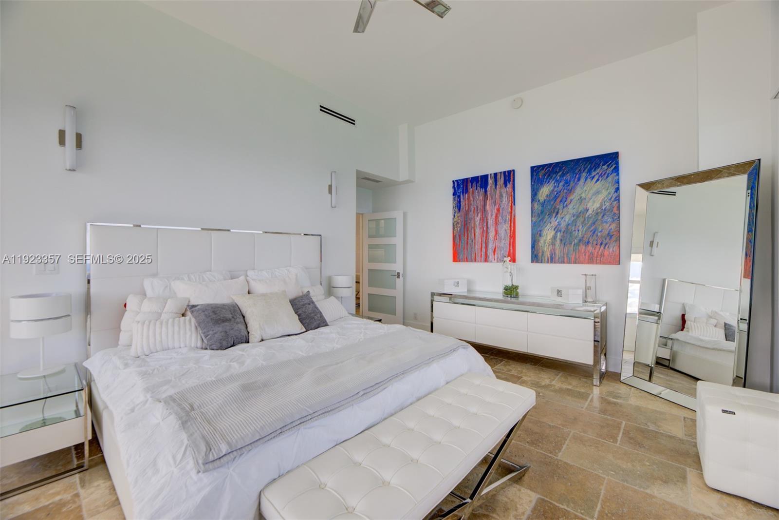 A modern bedroom features a white tufted headboard, a mirrored dresser, and stone tile flooring — 3725 S Ocean Dr, Hollywood FL 33019, HOLLYWOOD, FL