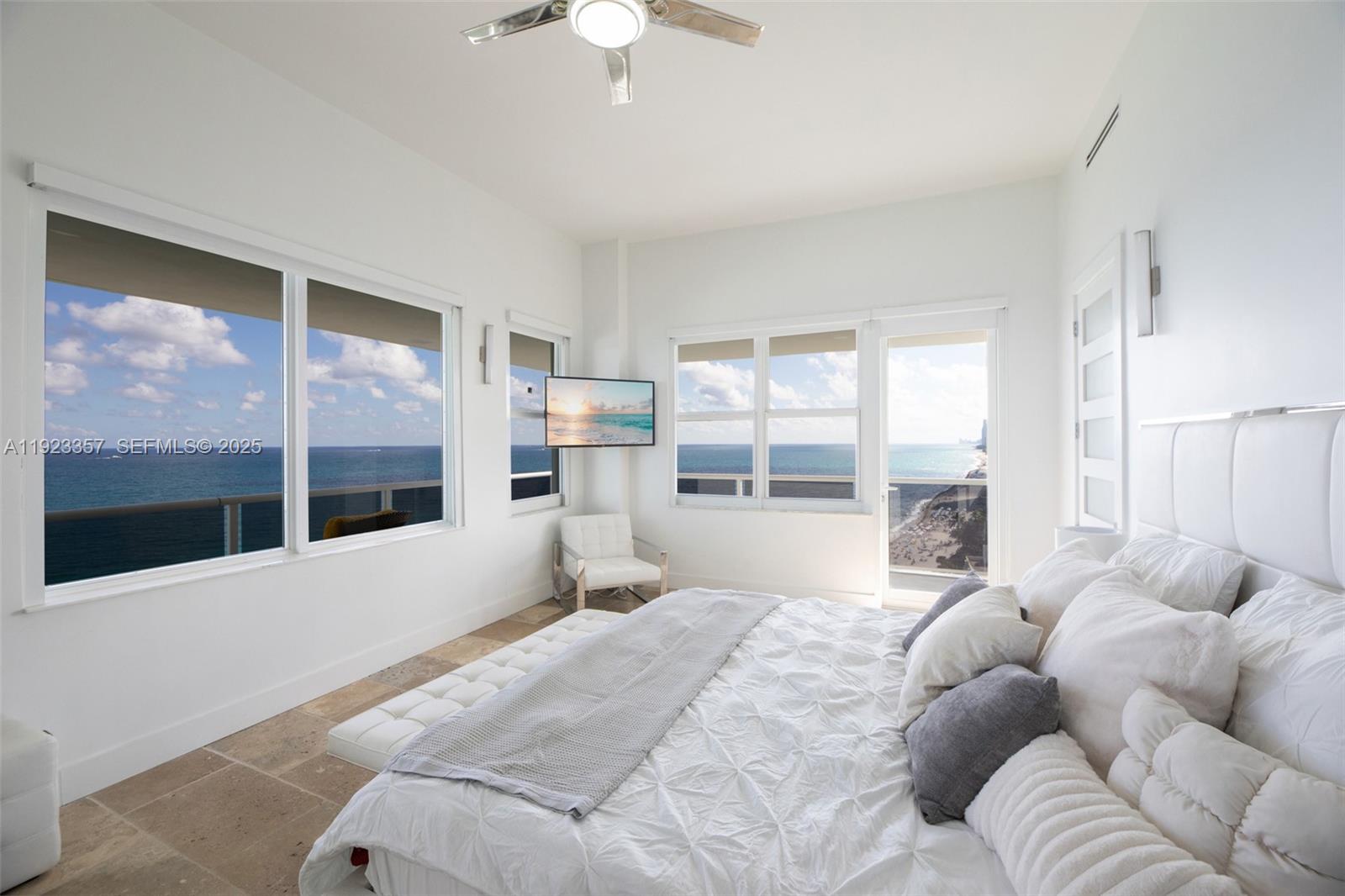 A bright bedroom features a white bed, tiled floors, and large windows overlooking the ocean — 3725 S Ocean Dr, Hollywood FL 33019, HOLLYWOOD, FL